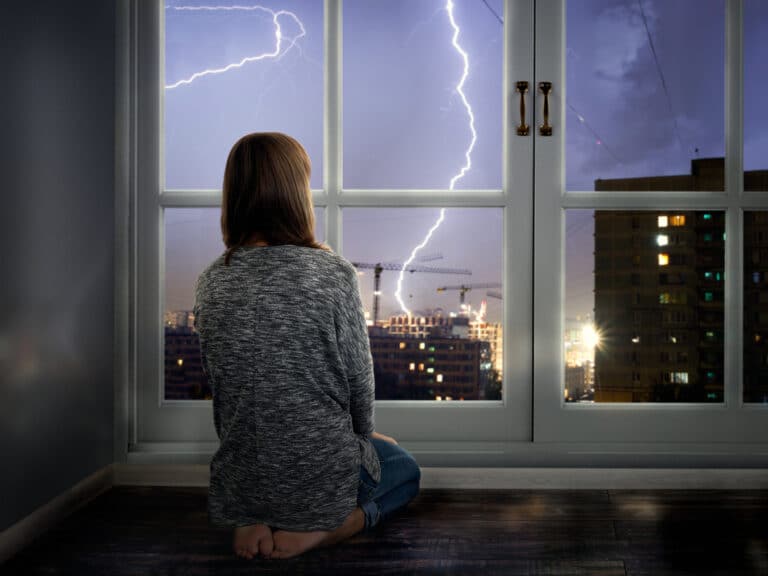 femme regarder fenêtre appartement ville orage peur tempête