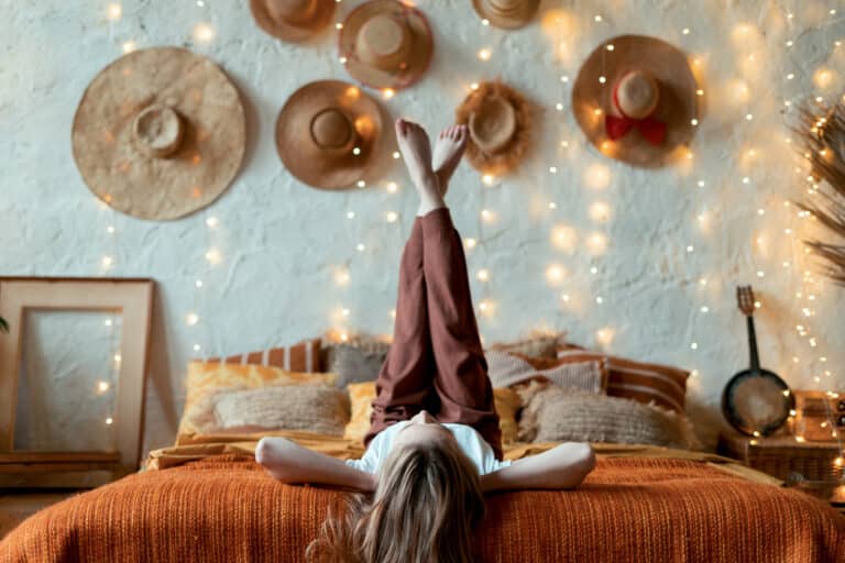 jeune femme lit allongée chandelle déco chambre chapeaux mur guirlandes lumineuses